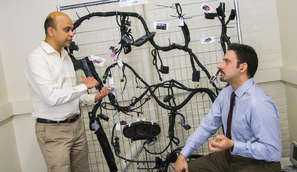Alex Wyglinski and Raghvendra Cowlagi discuss the technology involved in autonomous vehicles, with a wiring harness for a 2014 Chevy Impala in the background. 