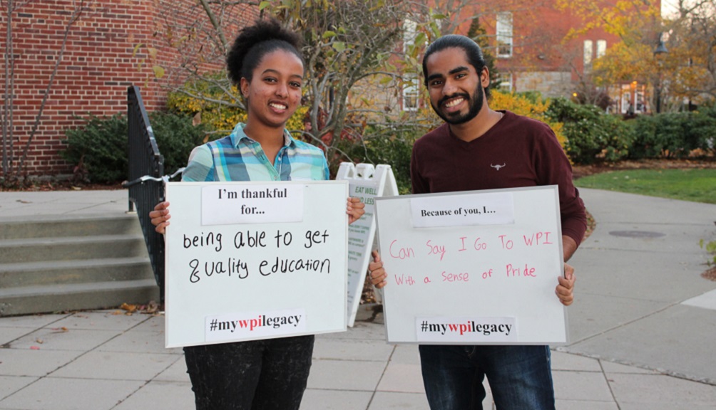 Two students smile while holding up signs that read: "I'm thankful for being able to get a quality education" and "Because of you, I can say I go to WPI with a sense of pride."