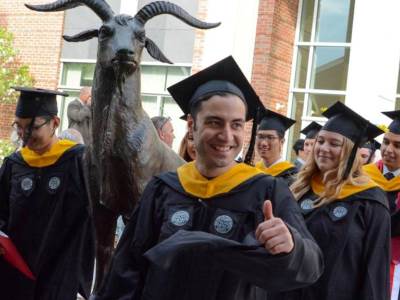 A student in a black robe gives the thumbs up as he passed the Proud Goat statue