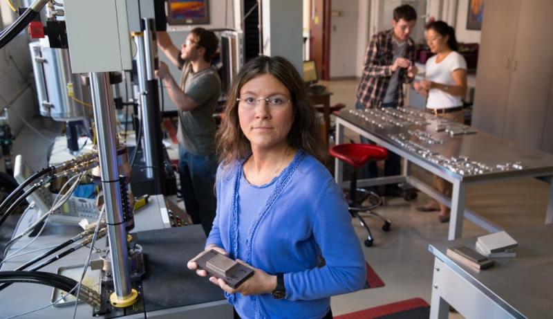 Diana Lados, in the materials testing laboratory, faces the camera and holds a part made with additive manufacturing