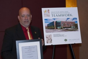 Fred DiMauro holds the Build New England award, standing next to a rendering of the Faraday residence hall.