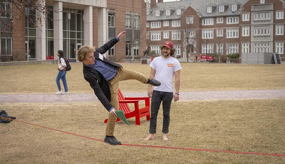 A student balances on a tightrope along the quad.