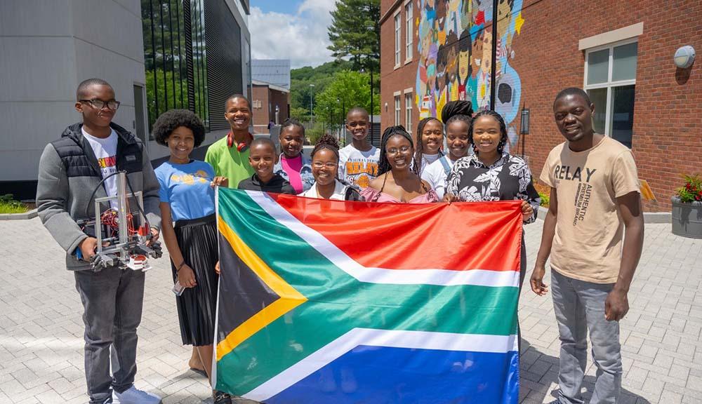 Robotics team members from Worcester, South Africa, show off their country’s flag and one of the robots they brought to WPI.