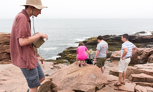 Students observe the ocean from the top of a rocky mountain peak.