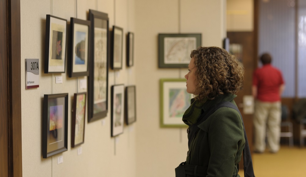 In a shot from the side, a woman in a green sweater looks at some art on display in the Gordon Library.