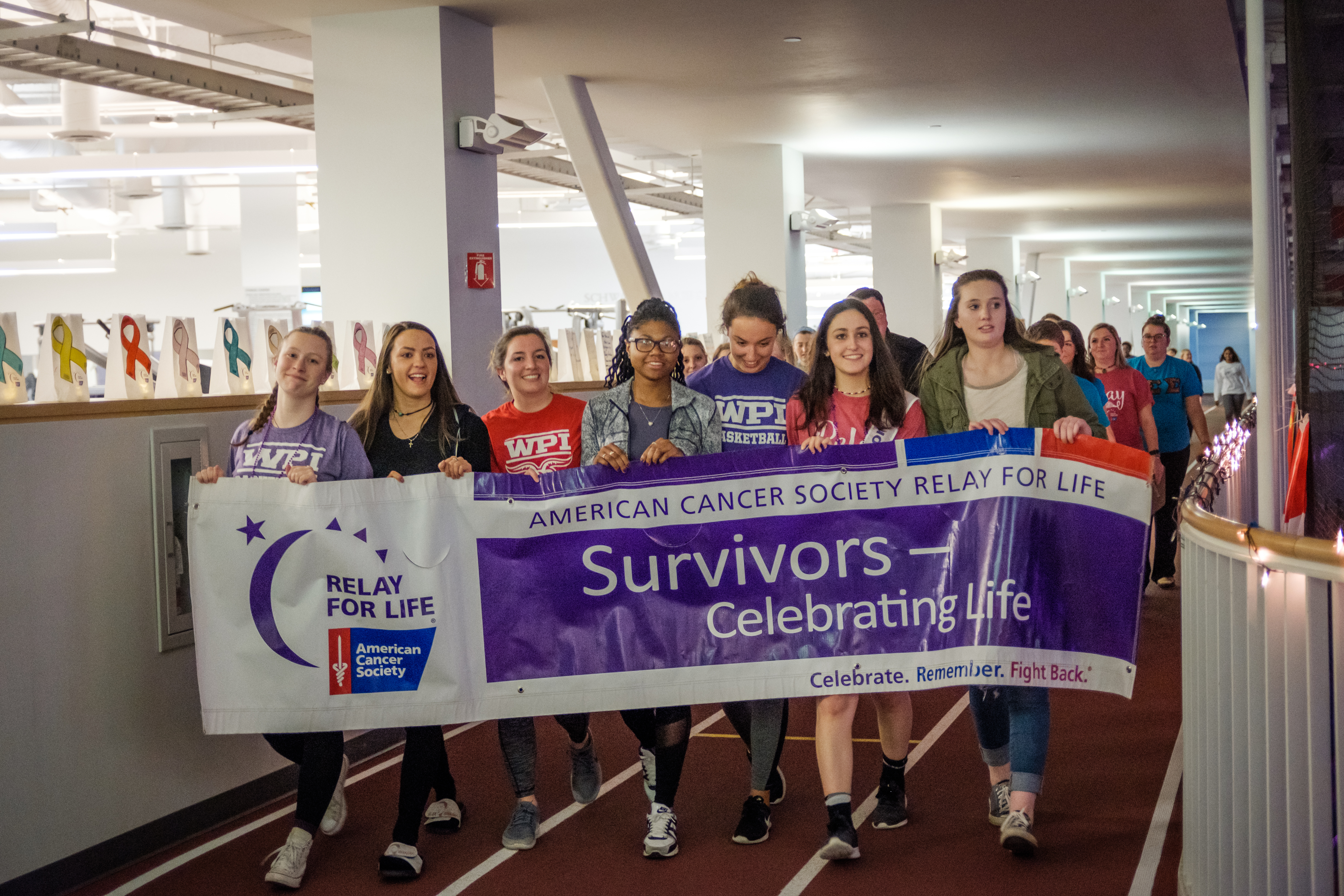 Several students walk around the indoor track together, holding a banner that says "Survivors: Celebrating Life."