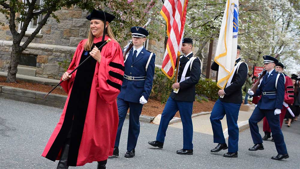 Dressed in red and black commencement regalia, Natalie Farny leads students along the processional toward the Quad.