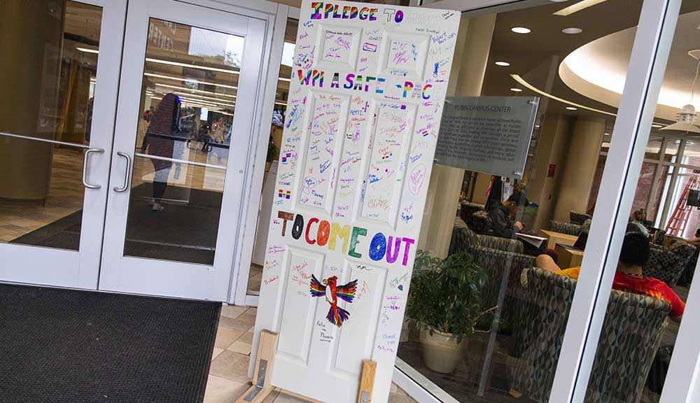 A white door in the Rubin Campus Center with "I Pledge to Make WPI a Safe Space to Come Out" written on it with signatures in rainbow colors.