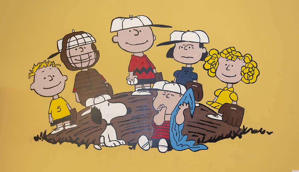 A close up photo of a mural of the Peanuts gang on a mustard yellow background.