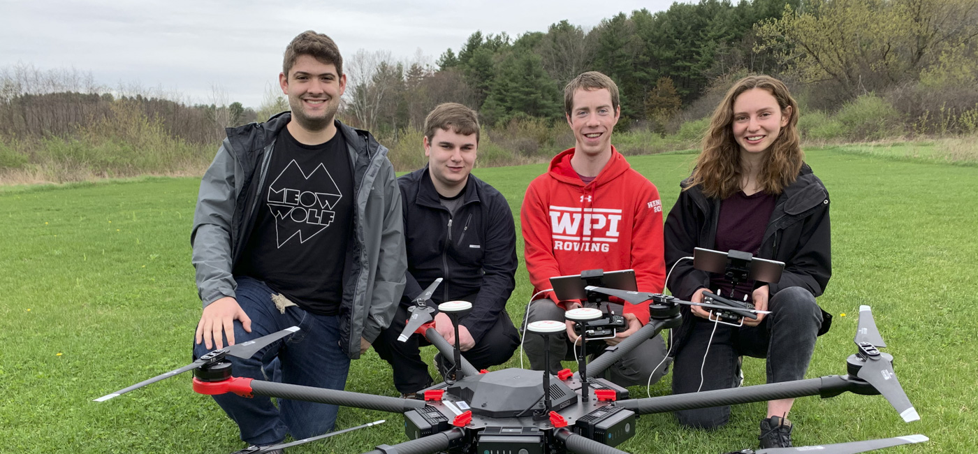 Four WPI students posing in a grassy field with an industrial drone