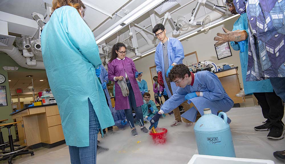 Students in the Frontiers program participate in a lab experiment with fog rolling around their feet.
