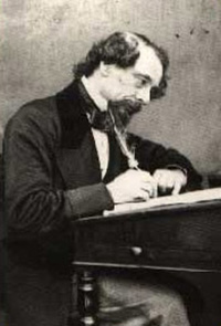 Photo of Charles Dickens sitting a desk writing with a quill pen
