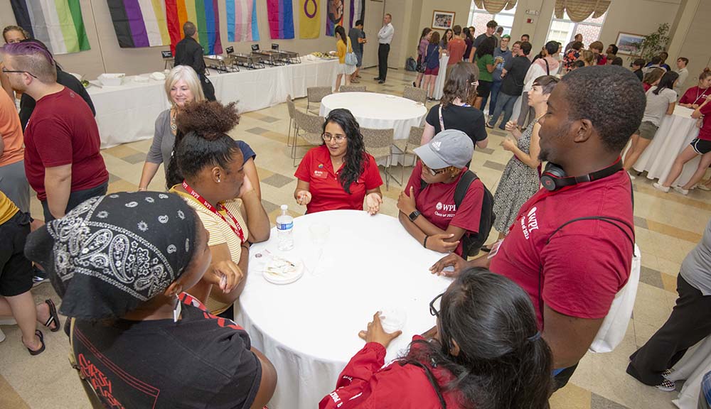 Students and staff gather around a table during one of the Office of Multicultural Affairs' welcome events. A variety of pride flags are hanging on the wall in the background.