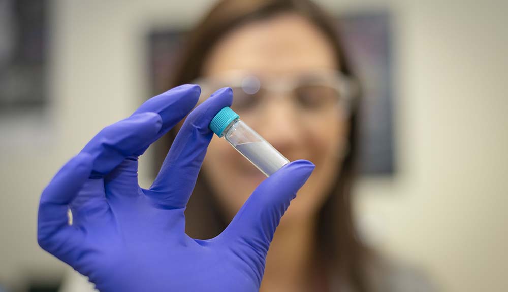A gloved hand holds a vial of cold spray technology being used by researchers.