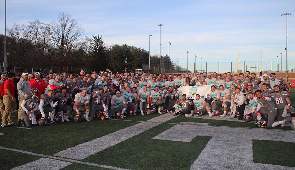 The football team gathers for a photo on the field holding a championship banner among them.