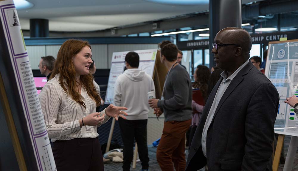 Provost Wole Soboyejo listens to a student present her work on a poster during Next-in-Bio.
