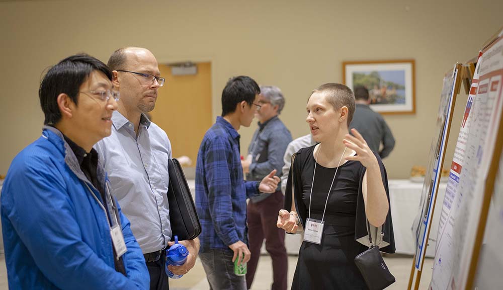 A grad student discusses her work on her poster board with members of the WPI community during GRIE.