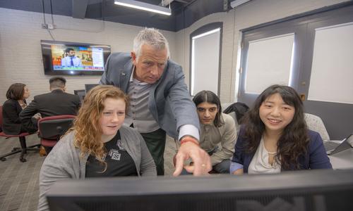 three students and one professor looking at a screen with two students sitting in the background