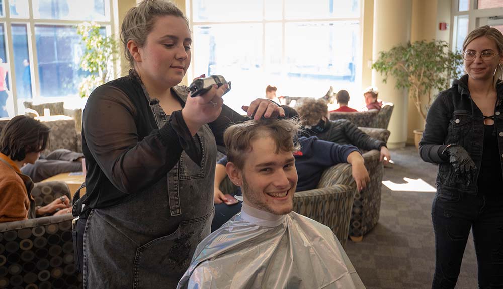A student smiles as he gets his head shaved in the Rubin Campus Center.