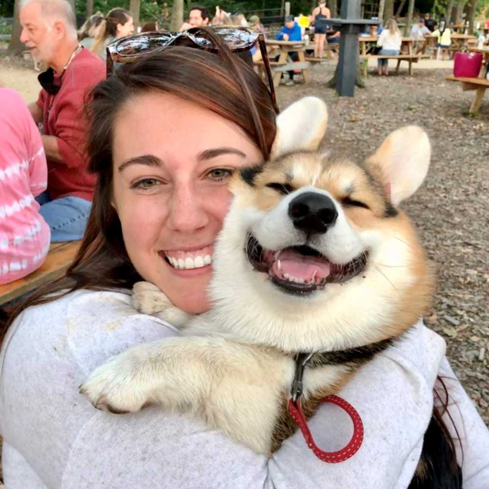 Brianna smiles while holding her corgi, who is also smiling.