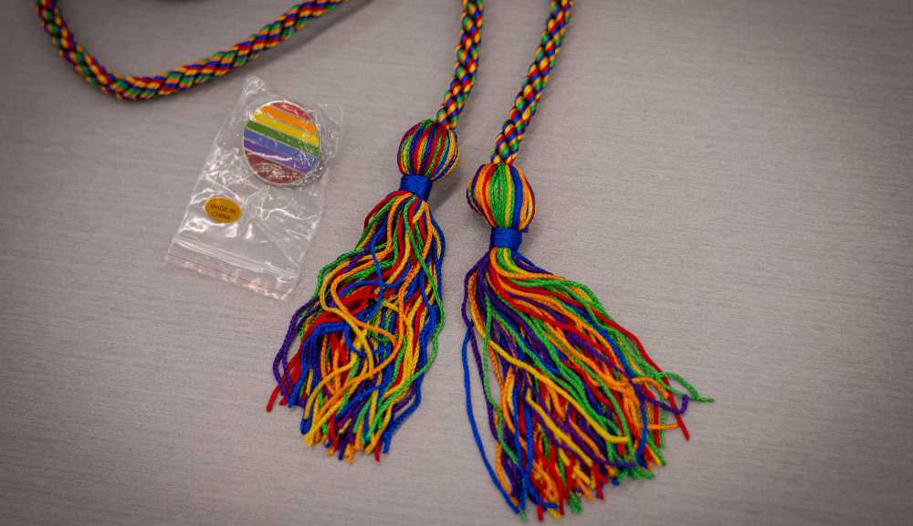 A close-up photo of a rainbow pin and rainbow graduation cords.