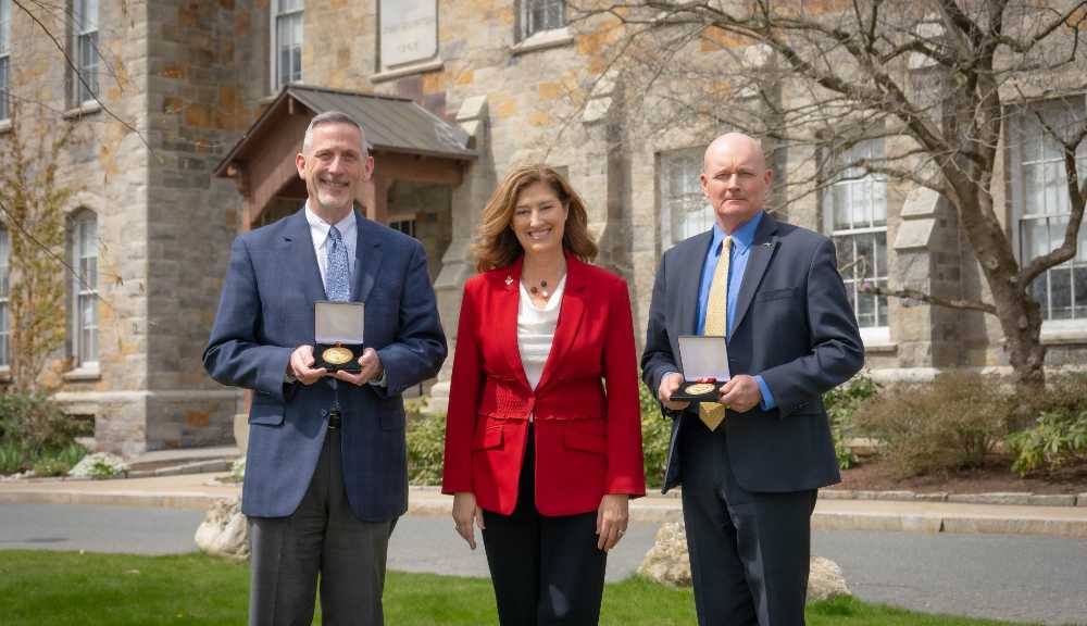Philip Clay, Laurie Leshin, and Ron Bashista stand outside of Boynton Hall, with Clay and Bashista holding presidential medals.