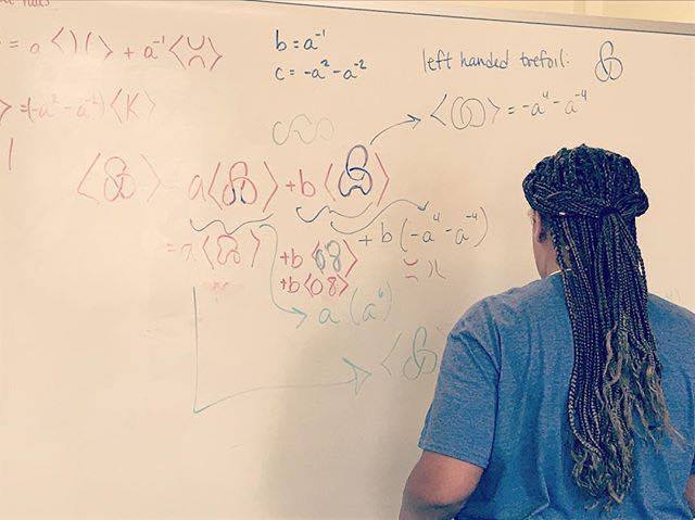 Girls Talk Math camper facing a white board with knot theory calculations. alt