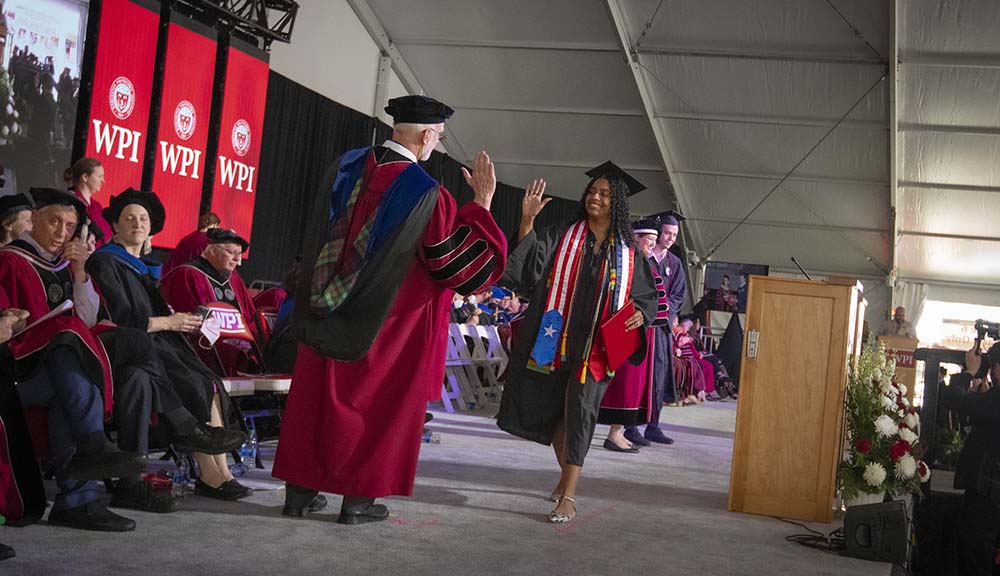 A graduate offers a high five while crossing the commencement stage.