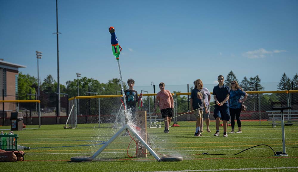 Students watch as a water rocket launches into the air.