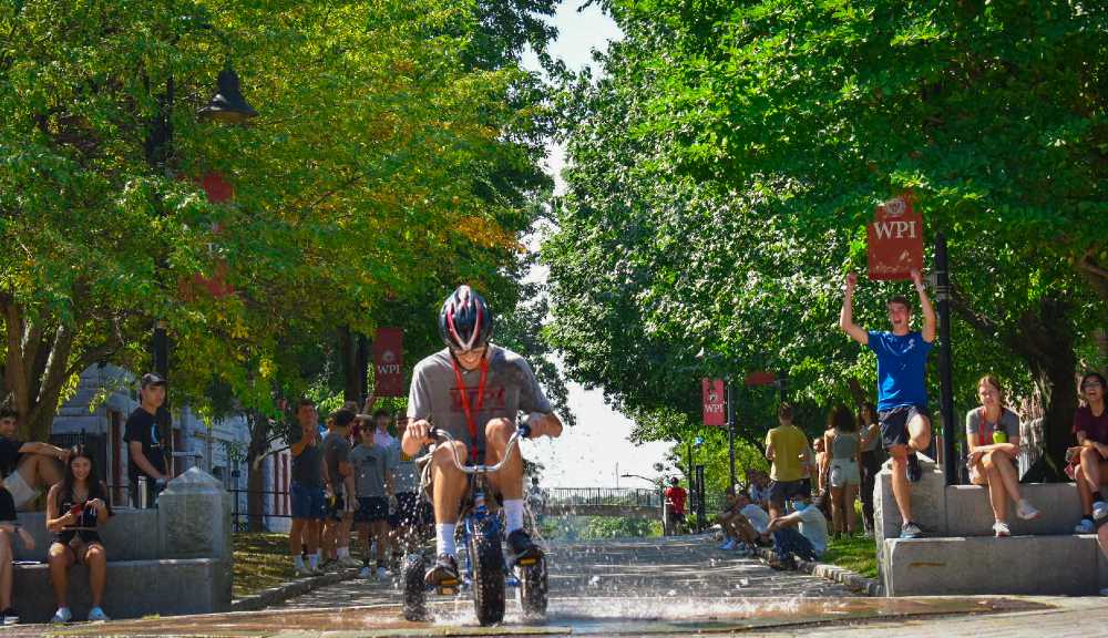 A student pedals a trike through the fountain during Orientation Olympics.