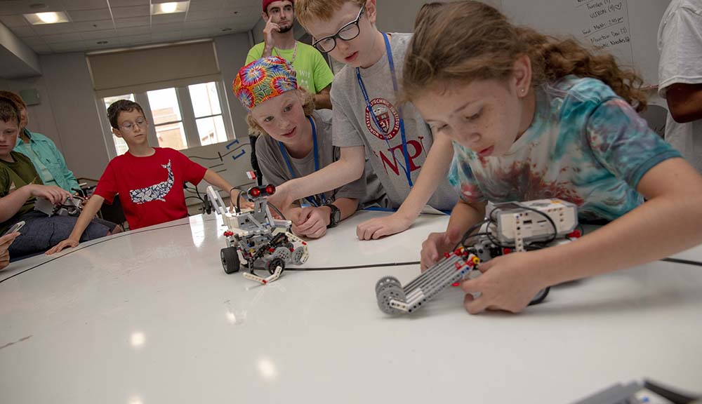 One student works on a small robot while two others look on.