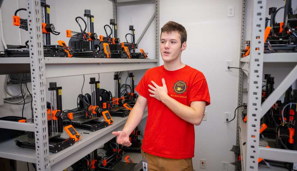 Ezekiel “Zeke” Andreassen ’22 stands next to a shelf of 3D-printed robot parts in Unity Hall.