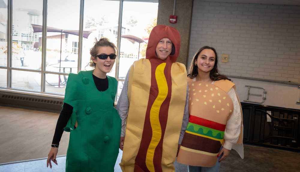 Members of the WPI community pose in their Halloween costumes: a pickle, a hot dog, and a hamburger.