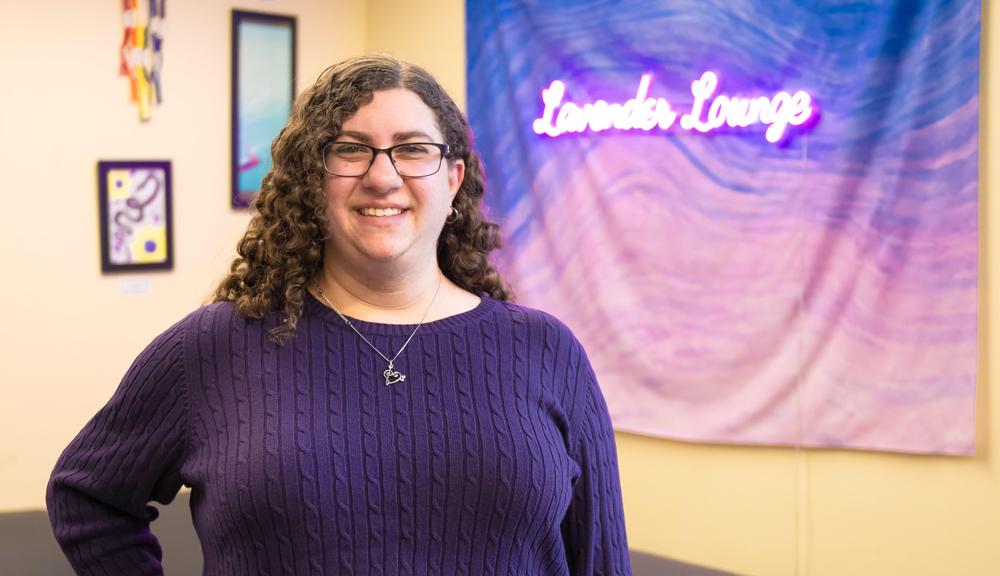 Lauren Feldman standing in front of a neon purple sign for the Lavender Lounge
