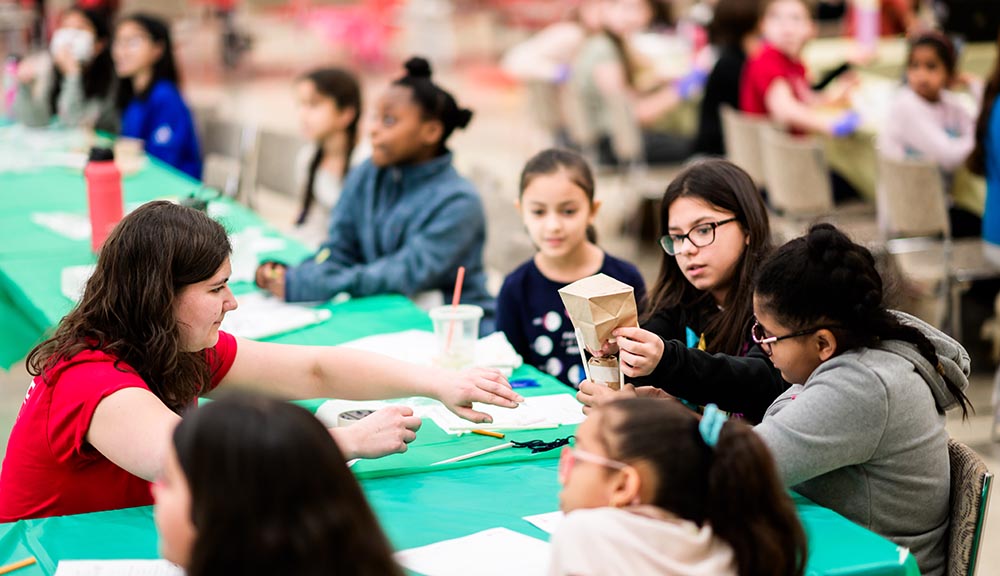 An engineering ambassador works with a group of young girls on a STEM experiment.