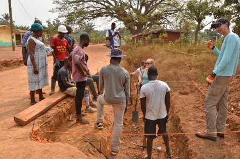 people working on a project together outside around a sandy area digging a hole
