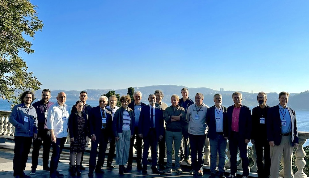 Electrical engineering educators pose for a group photo with a blue sky, mountains, and body of water in the background
