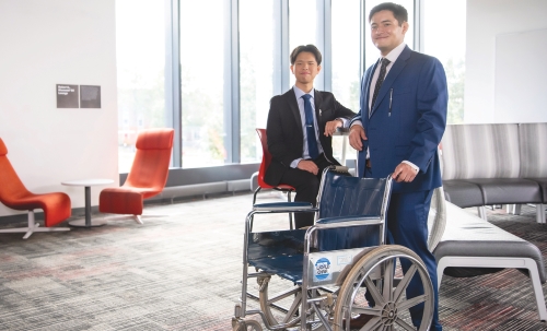 Students dressed in suits posing in front of a wheelchair