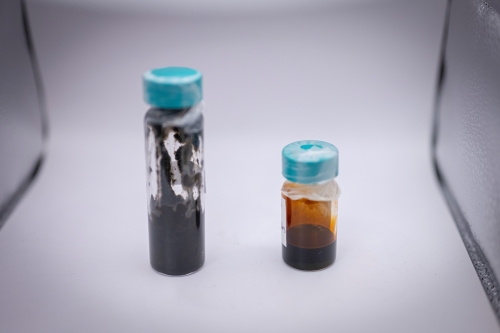 Liquids in two test tube vials, placed on a lab bench in front of a white background