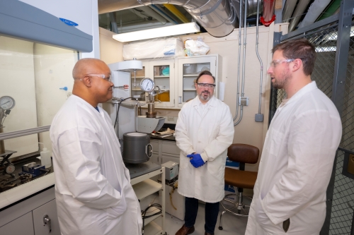 Three researchers standing together in front of a gray drape. Professor Yunus Telliel on the left wearing a black shirt, Professor Robert Dempski in the middle wearing a white shirt, PhD student Max Chen on the right wearing a brown jacket.