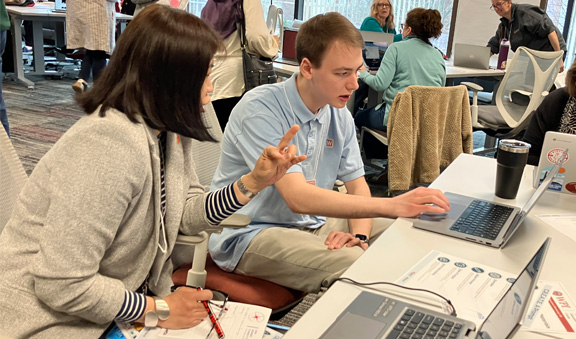 Participants work together at a laptop at a workshop session.
