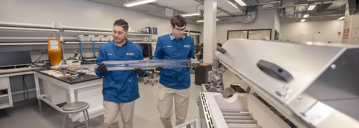 Two students carry a large device inside a lab at WPI
