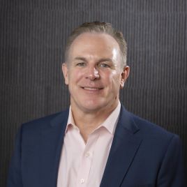 Thomas Driscoll headshot in a suit jacket and pink button down shirt