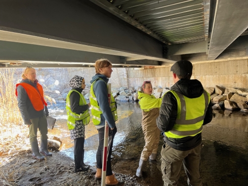 Students under a bridge looking at a waterway.