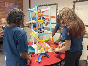 Seventh grade students combining creativity and engineering in math class brainstorming, designing, building, and testing roller coasters.
