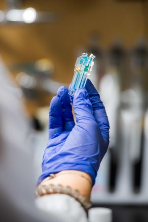 The gloved hand of a researcher holds a clear container that holds a blue liquid.