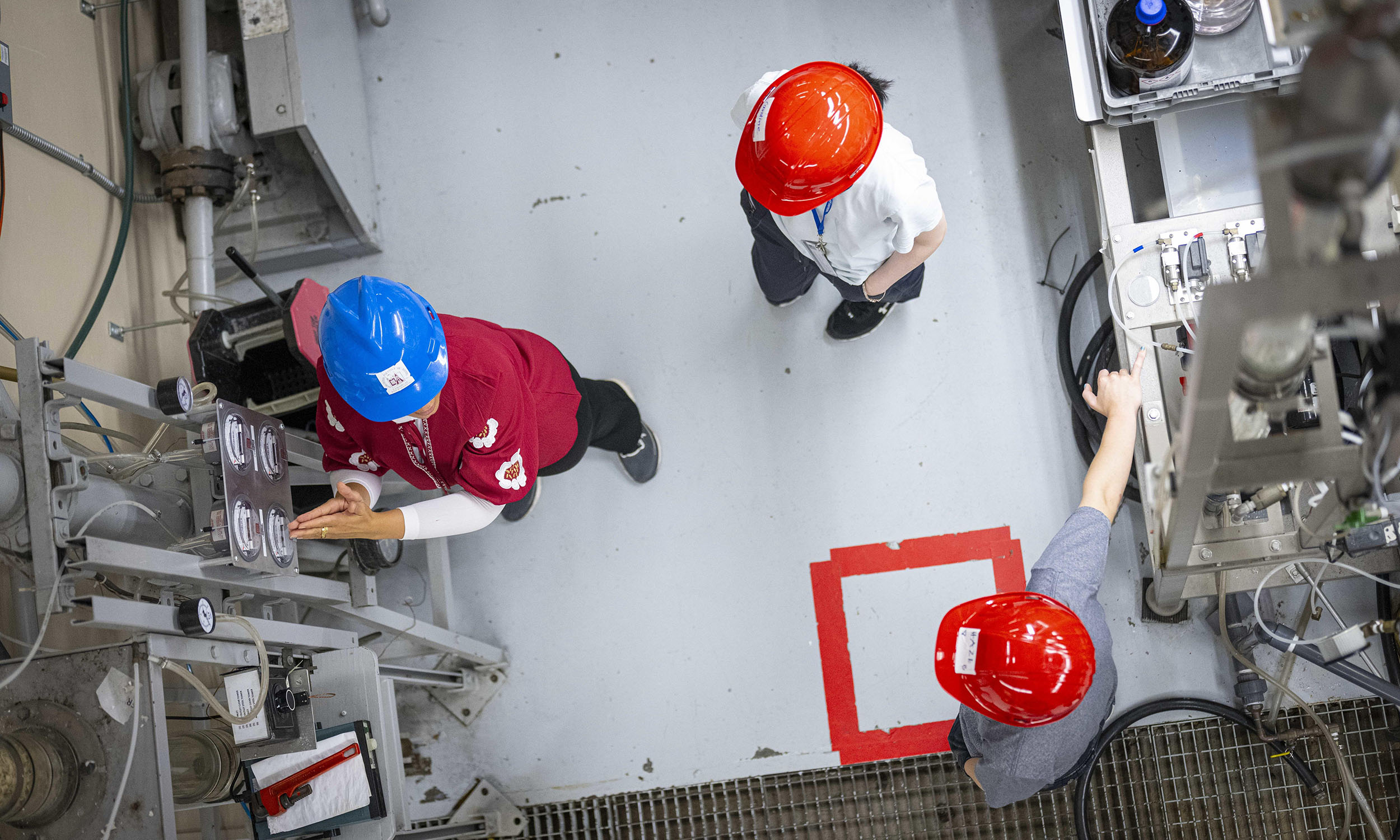 Photo looking down at students and a professor wearing hard hats in a factory setting