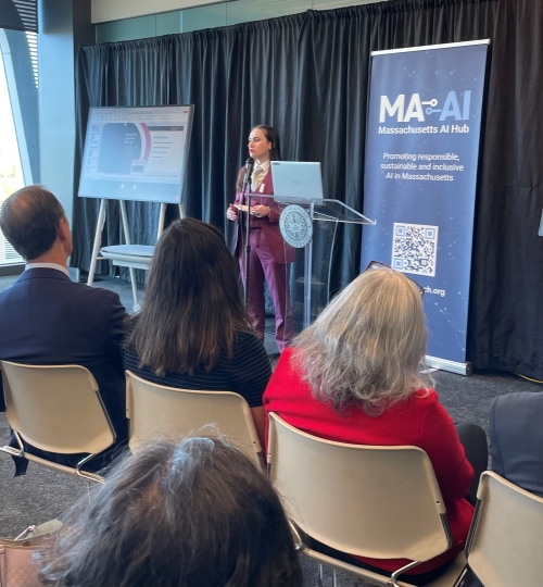 PhD student speaking in front of a room at a podium with a powerpoint presentation on a screen behind them