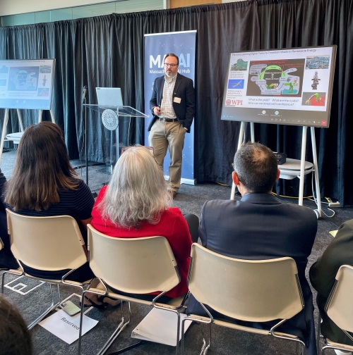 Professor speaking at a podium in front of a crowd with powerpoint slides on a screen behind him.