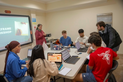 Students sitting around a table working on computers in a group.